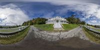 an old mansion surrounded by greenery with trees and clouds above it in a circular fisheye effect effect