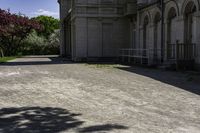 a picture of a driveway lined with trees and buildings behind it and a bench on either side of the area