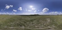 a panorama - lens image of grass and the sun in the sky on a sunny day