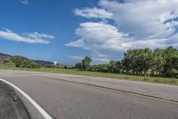 an empty road with yellow line markers leading into a grassy green area and a blue sky