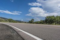 an empty road with yellow line markers leading into a grassy green area and a blue sky