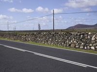 a single vehicle is traveling along an empty road in a remote area with telephone lines