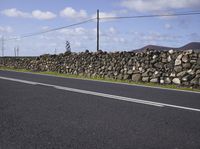 a single vehicle is traveling along an empty road in a remote area with telephone lines