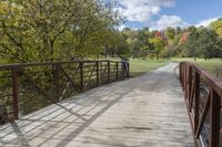 a wooden bridge over a paved path in the autumntime with fall foliage and a path winding through it