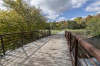 a wooden bridge over a paved path in the autumntime with fall foliage and a path winding through it