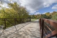 a wooden bridge over a paved path in the autumntime with fall foliage and a path winding through it