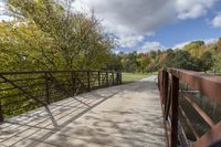 a wooden bridge over a paved path in the autumntime with fall foliage and a path winding through it