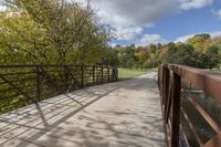 a wooden bridge over a paved path in the autumntime with fall foliage and a path winding through it