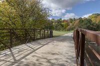 a wooden bridge over a paved path in the autumntime with fall foliage and a path winding through it