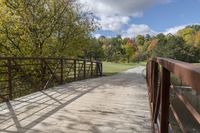 a wooden bridge over a paved path in the autumntime with fall foliage and a path winding through it