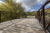 a wooden bridge over a paved path in the autumntime with fall foliage and a path winding through it