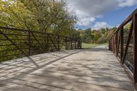 a wooden bridge over a paved path in the autumntime with fall foliage and a path winding through it