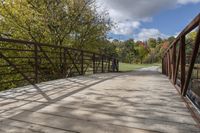 a wooden bridge over a paved path in the autumntime with fall foliage and a path winding through it