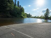 a car parked along the bank of a river while the sun shines through trees