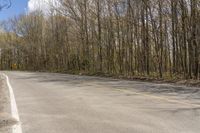 a road with no vehicles and trees with no leaves on it, near some hills