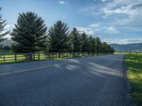 a empty road that goes through a grassy area with mountains in the background as well as trees