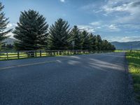 a empty road that goes through a grassy area with mountains in the background as well as trees