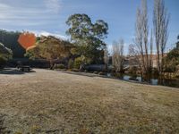 a sunny day in a park with a river and picnic tables, trees and grass