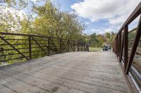 a wooden bridge over a paved path in the autumntime with fall foliage and a path winding through it