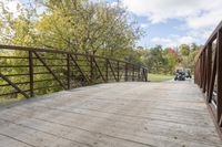 a wooden bridge over a paved path in the autumntime with fall foliage and a path winding through it