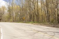 a yellow and white sign by the road in the woods next to trees and bushes