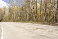 a yellow and white sign by the road in the woods next to trees and bushes