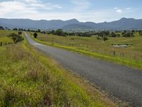 a countryside with a wide road, fields and mountains in the background, along a gravel path