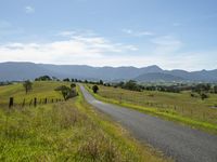 a countryside with a wide road, fields and mountains in the background, along a gravel path