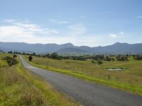 a countryside with a wide road, fields and mountains in the background, along a gravel path