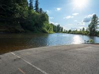 an empty road with two cars on each side of the road that is by a lake in a wooded area