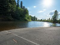 an empty road with two cars on each side of the road that is by a lake in a wooded area