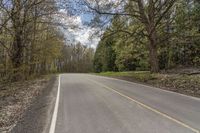 a person riding a motorcycle down a narrow road past some trees on both sides of it