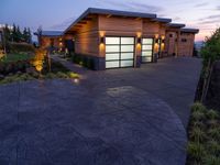 concrete driveway in front of modern, home entrance with glass door and lights on at twilight