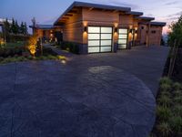 concrete driveway in front of modern, home entrance with glass door and lights on at twilight