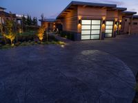 concrete driveway in front of modern, home entrance with glass door and lights on at twilight