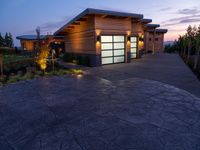 concrete driveway in front of modern, home entrance with glass door and lights on at twilight