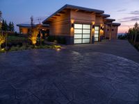 concrete driveway in front of modern, home entrance with glass door and lights on at twilight