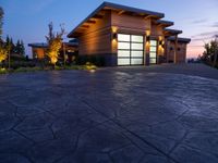 concrete driveway in front of modern, home entrance with glass door and lights on at twilight