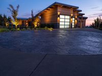 concrete driveway in front of modern, home entrance with glass door and lights on at twilight