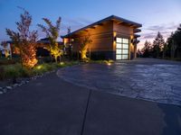 concrete driveway in front of modern, home entrance with glass door and lights on at twilight