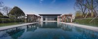 the outdoor swimming pool with several lounges sits next to the home's large glass - framed entry