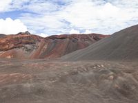 a black and red mountain with a few clouds in the sky above it and some brown hills