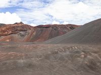 a black and red mountain with a few clouds in the sky above it and some brown hills