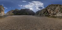 a fish eye view of the mountains and water near some rocks on a beach with some grass