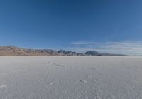 snowboarder looking up at vast expanse in desert area with mountain range in background