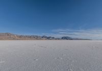 snowboarder looking up at vast expanse in desert area with mountain range in background