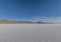 snowboarder looking up at vast expanse in desert area with mountain range in background