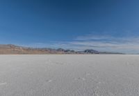 snowboarder looking up at vast expanse in desert area with mountain range in background