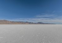 snowboarder looking up at vast expanse in desert area with mountain range in background