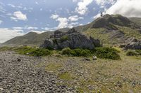 a person is taking photos on their cell phone at the top of a mountain near some rocks and scrubby